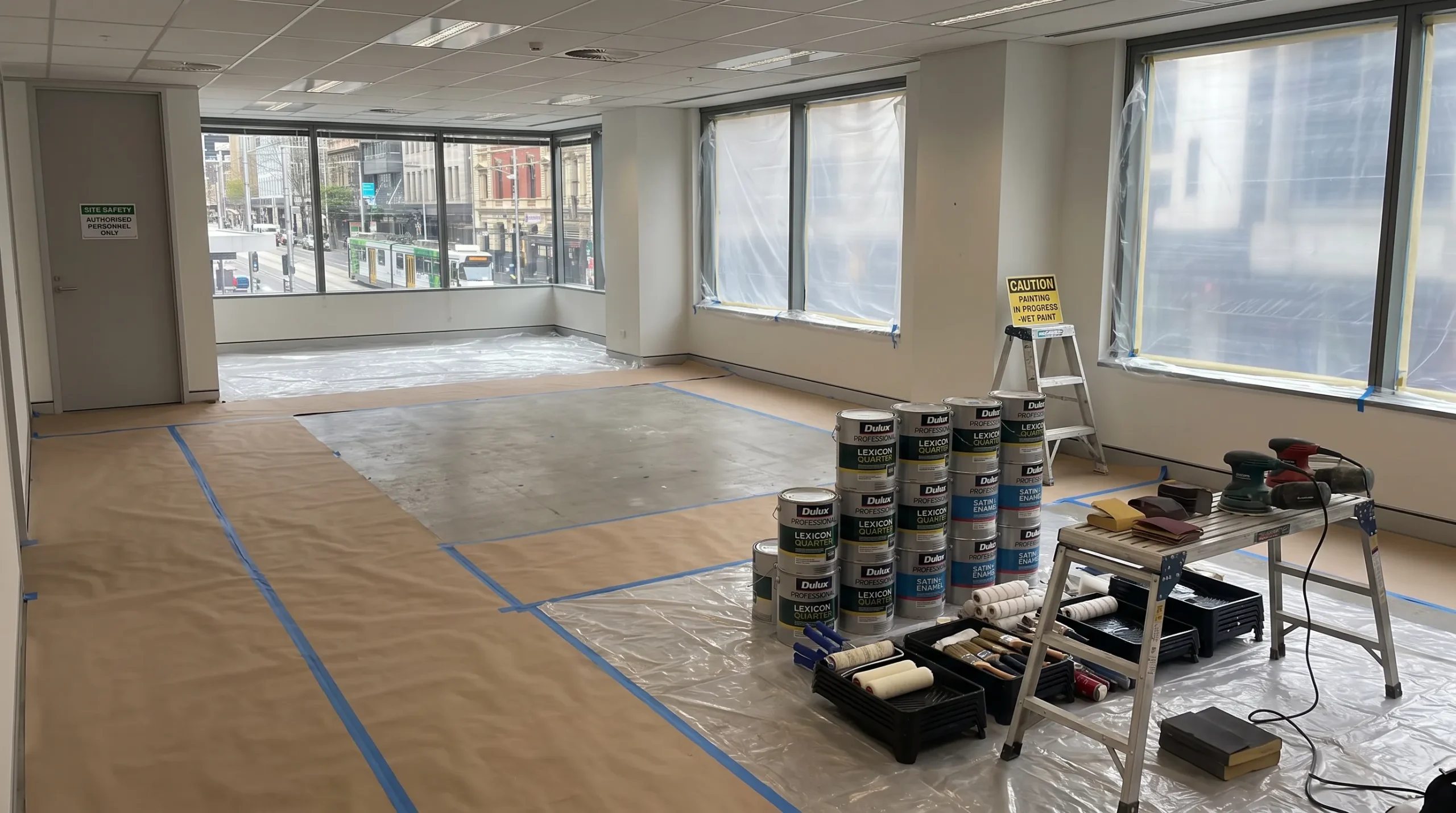A Melbourne commercial workspace is set up for repainting with protected floors, masked windows, paint tins and organised tools.