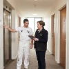 A building manager and painting contractor inspect a shared apartment corridor before planning work on its walls and common areas.