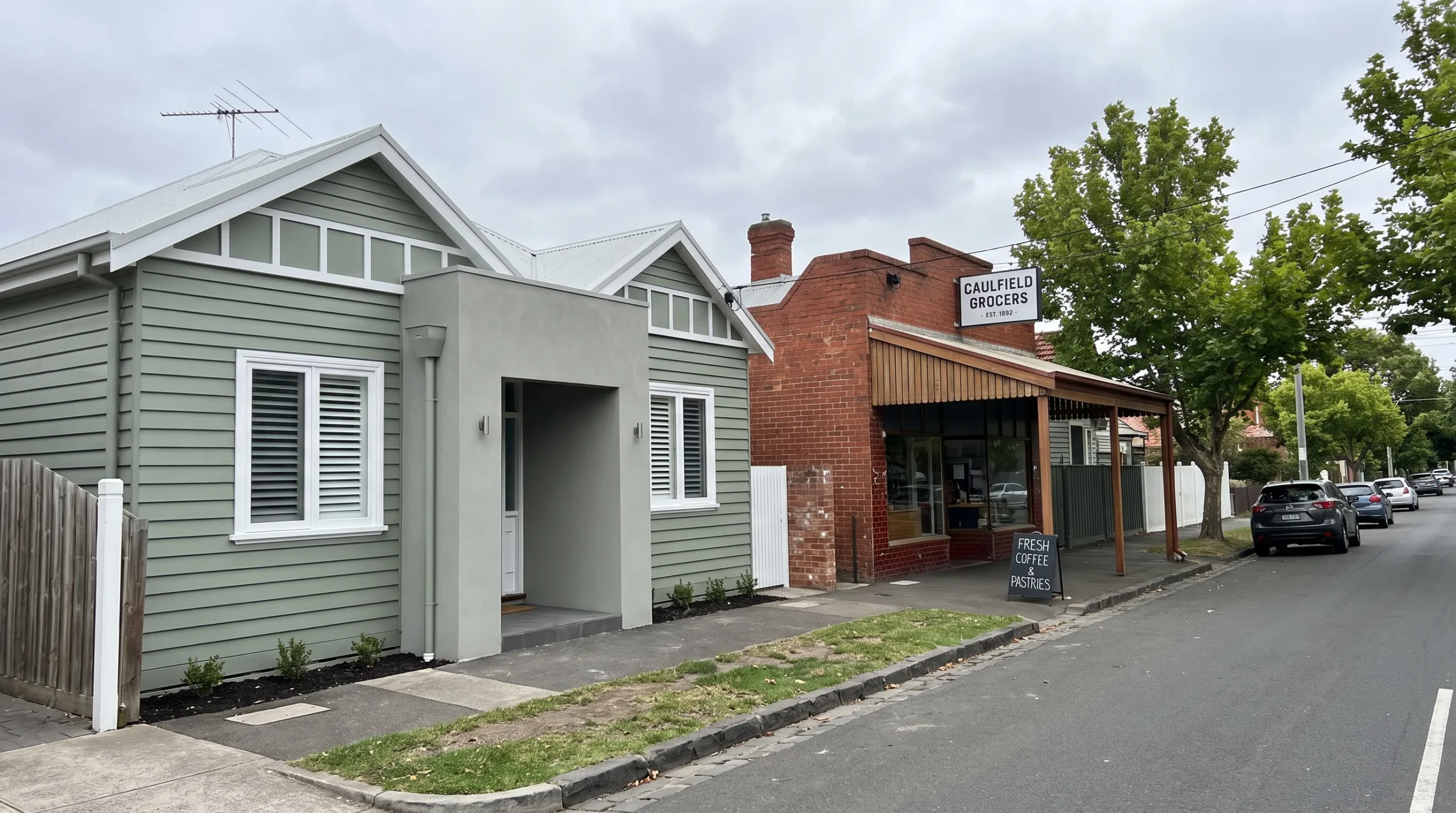 A freshly painted weatherboard home stands beside a small brick shopfront on a Melbourne streetscape, showing finished timber window frames, exterior trim and rendered entrance surfaces.