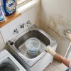 A homeowner cleans grime from a laundry wall above the utility sink before repainting.