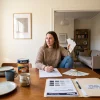 A homeowner sorts paint and care information at the dining table after a house repaint.