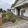 A Melbourne homeowner surveys the exterior of a weatherboard house before comparing painting companies.