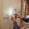 A painter measures damaged wall areas in a hallway to assess preparation before quoting a Melbourne home.