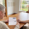 A painting contractor discusses the listed surfaces and costs with a homeowner at a dining table.