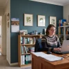 A person works at a desk against a muted feature wall in a home office connected to the rest of the house.