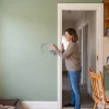 A resident gently wipes a kitchen wall in a freshly painted Melbourne home, with the doorway and everyday kitchen furnishings nearby.