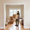 A tenant carries a box into a freshly painted Melbourne apartment, where neat walls and trim give the home a cared-for appearance.