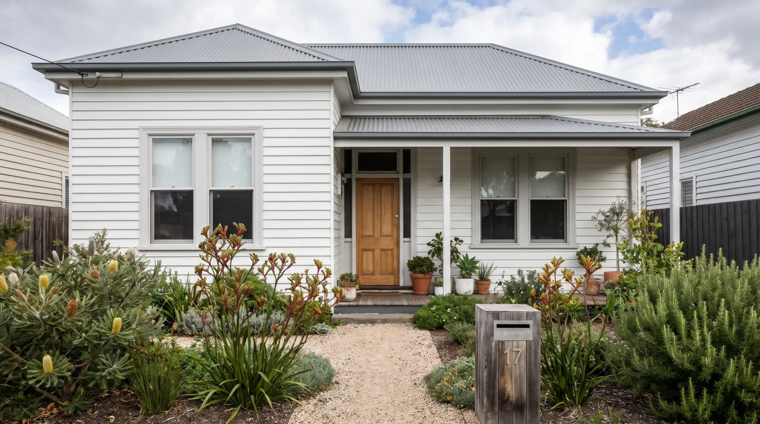 A white weatherboard Melbourne home with grey roofing, matching window trim and an established garden after exterior painting.