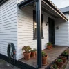 Freshly painted weatherboards run along a Melbourne home's verandah and side yard, with garden pots and a hose nearby.